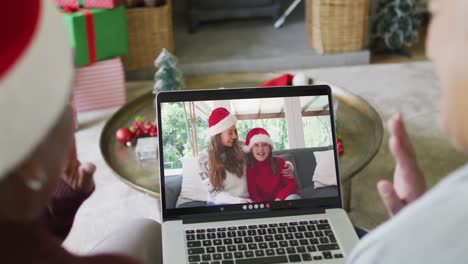 Diverse-senior-female-friends-using-laptop-for-christmas-video-call-with-happy-family-on-screen