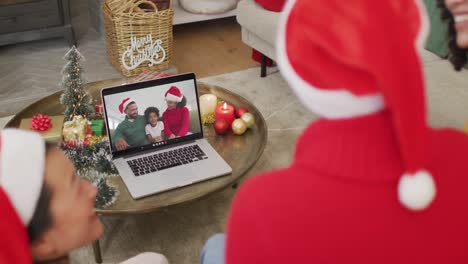 Vielfältige-Familie-Mit-Weihnachtsmützen-Und-Laptop-Für-Weihnachtsvideoanruf-Mit-Glücklicher-Familie-Auf-Dem-Bildschirm