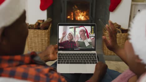 Afroamerikanisches-Paar-Mit-Weihnachtsmützen-Nutzt-Laptop-Für-Weihnachtsvideoanruf-Mit-Der-Familie-Auf-Dem-Bildschirm