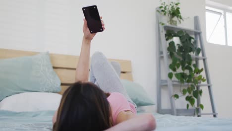 Asiatische-Frau,-Die-Morgens-Auf-Dem-Bett-Liegt-Und-Ihr-Smartphone-Mit-Kopierplatz-Benutzt