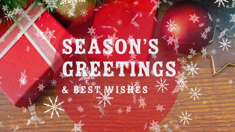 Animation-of-season's-greetings-text-over-snow-falling-and-christmas-decorations-on-table