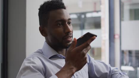 Worried-african-american-businessman-sitting-in-armchair-talking-on-smartphone-in-modern-office
