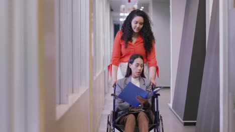 Happy-biracial-businesswoman-with-disabled-colleague-in-wheelchair-working-together-in-modern-office
