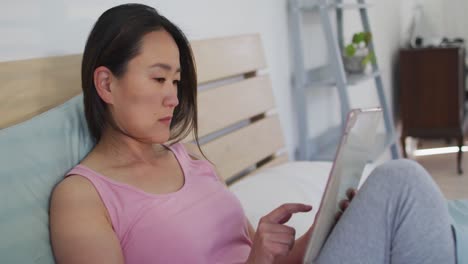 Fokussierte-Asiatische-Frau,-Die-Im-Bett-Liegt-Und-Morgens-Ein-Tablet-Benutzt