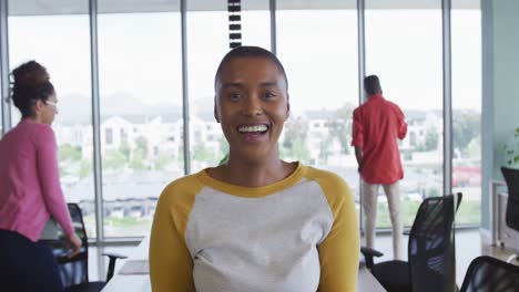 Lächelnde-Afroamerikanische-Kreative-Geschäftsfrau-Im-Büro,-Mit-Verschiedenen-Kollegen-Im-Hintergrund