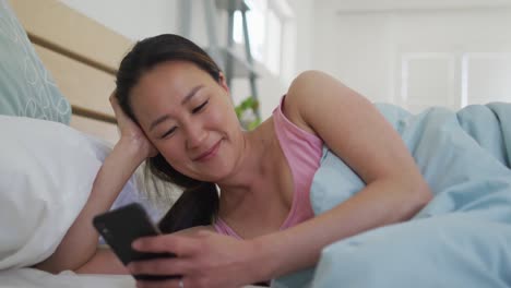 Glückliche-Asiatische-Frau,-Die-Morgens-Im-Bett-Liegt-Und-Ihr-Smartphone-Benutzt