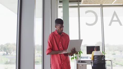 African-american-creative-businessman-standing-with-laptop-in-modern-interiors