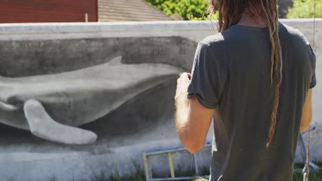 Video-of-caucasian-male-artist-with-dreadlocks-taking-photo-of-whale-mural-with-smartphone