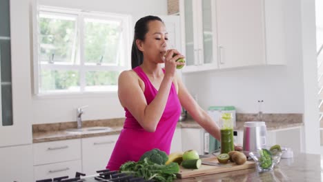 Relaxed-asian-woman-drinking-smoothie-in-kitchen