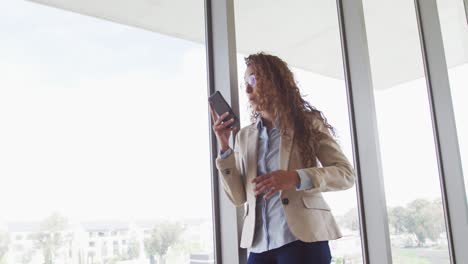 Biracial-businesswoman-smiling-and-talking-on-smartphone-in-modern-interiors