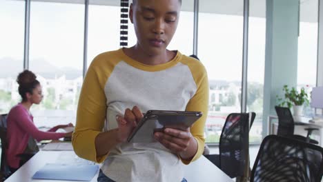 Afroamerikanische-Kreative-Geschäftsfrau-Nutzt-Tablet-Im-Büro,-Verschiedene-Kollegen-Im-Hintergrund