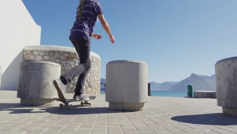 Video-Eines-Kaukasischen-Mannes-Mit-Dreadlocks,-Der-Auf-Der-Sonnigen-Strandpromenade-Skateboard-Fährt