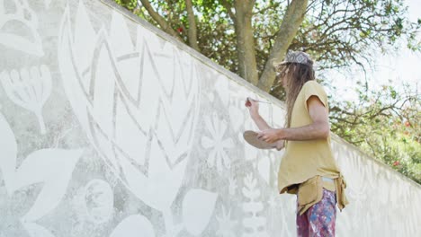 Video-of-caucasian-male-artist-with-dreadlocks-painting-mural-on-wall