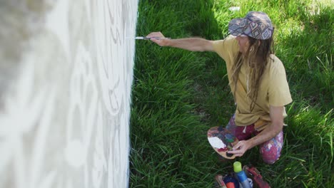 High-angle-video-of-caucasian-male-artist-with-dreadlocks-painting-mural-on-wall