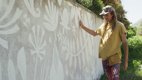 Video-of-caucasian-male-artist-with-dreadlocks-standing-touching-mural-on-wall