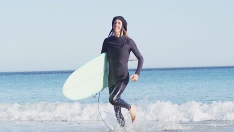 Video-of-smiling-caucasian-man-with-dreadlocks-in-wetsuit-carrying-surfboard-running-out-of-sea