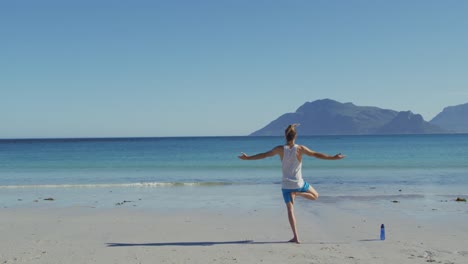 Video-of-rear-view-of-caucasian-man-with-dreadlocks-practicing-yoga-standing-on-sunny-beach