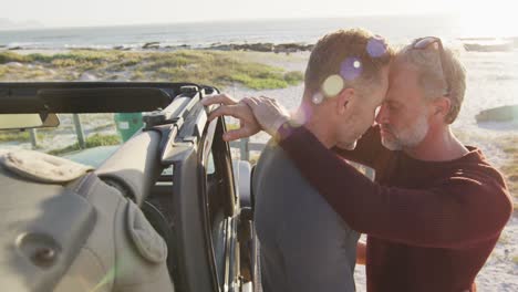 Happy-caucasian-gay-male-couple-standing-by-car-embracing-on-sunny-day-at-the-beach