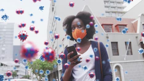 Animation-of-covid-19-cells-over-african-american-woman-in-face-mask-using-smartphone
