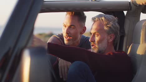 Happy-caucasian-gay-male-couple-sitting-in-car-admiring-the-view-and-talking-at-the-beach