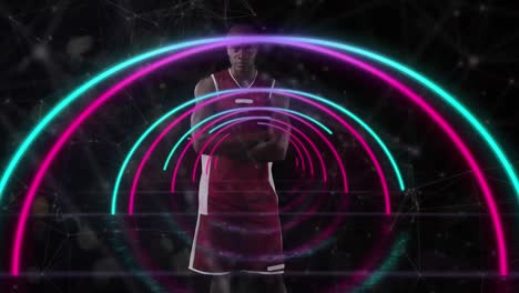 Animation-of-pink-and-blue-neon-arcs-and-network-over-waiting-male-basketball-player