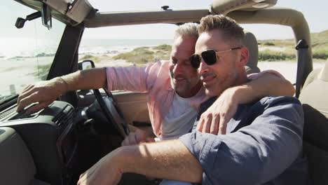Happy-caucasian-gay-male-couple-sitting-in-car-embracing-on-sunny-day-at-the-beach
