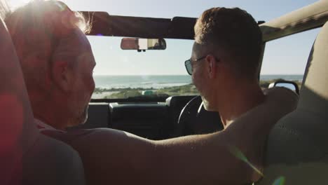 Happy-caucasian-gay-male-couple-sitting-in-car-and-embracing-on-sunny-day-at-the-beach