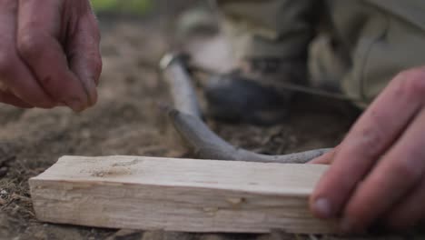 Hands-of-caucasian-male-survivalist-adding-dry-earth-to-prepare-fireboard-at-camp-in-wilderness