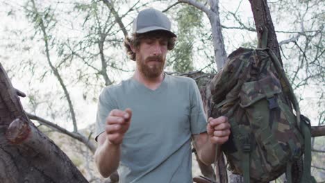 Bearded-caucasian-male-survivalist-untying-paracord-at-camp-in-wilderness