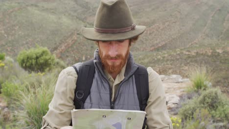 Bearded-caucasian-male-survivalist-on-mountain-in-wilderness,-reading-map-and-looking-around