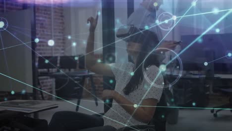 Animation-of-glowing-network-of-connections-over-woman-using-vr-headset-in-creative-office