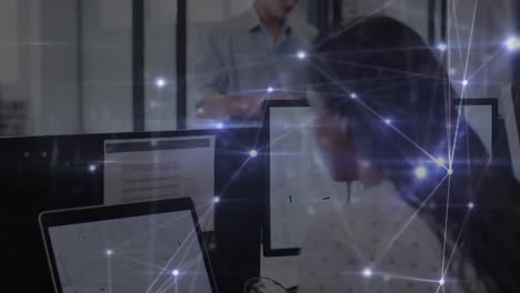 Animation-of-glowing-network-of-connections-over-woman-working-with-computers-in-office
