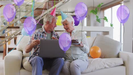 Glückliches-Kaukasisches-älteres-Paar-Mit-Partyhüten,-Das-Einen-Geburtstags-Laptop-Videoanruf-Mit-Kuchen-Und-Luftballons-Macht