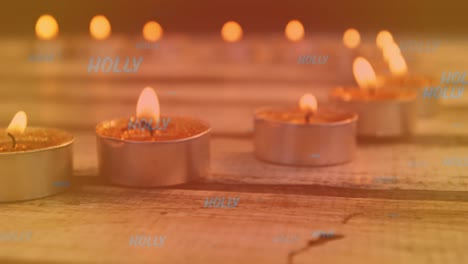 Animation-of-holly-text-in-blue-over-lit-tea-light-candles