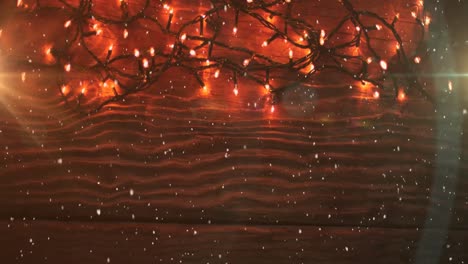 Animation-of-snow-falling-over-red-christmas-fairy-lights-on-wood