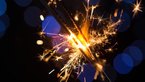 Animation-of-sparklers-and-blue-bokeh-lights-scrolling-on-black-background