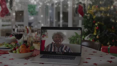 Animation-of-snow-falling-over-senior-woman-on-laptop-screen-making-christmas-video-call