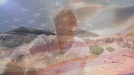 Animation-of-smiling-senior-caucasian-man-sitting-on-beach-over-flag-of-united-states-of-america