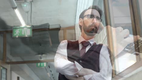 Animation-of-hands-using-laptop-over-businessman-looking-out-of-window-at-office