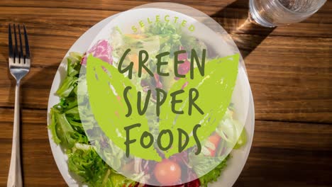Animation-Von-Grünem-Superfoods-Text-In-Grün-über-Einem-Teller-Mit-Frischem-Salat-Auf-Einem-Holztisch