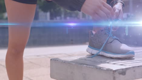Animation-of-blue-light-moving-over-feet-of-woman-in-shorts-tying-running-shoe