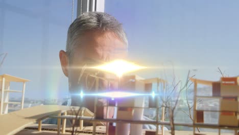 Animation-of-light-beams-and-lens-flare-over-male-architect-looking-at-architectural-model