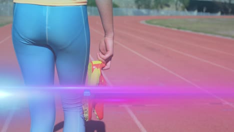 Animation-of-light-moving-over-midsection-of-woman-holding-running-shoes-walking-on-running-track