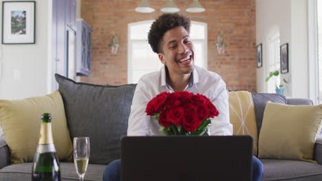 Happy-biracial-man-with-red-roses-making-valentine's-day-video-call-on-laptop