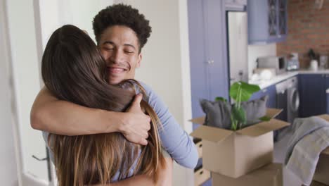 Happy-biracial-couple-moving-house,-embracing-and-smiling-in-kitchen