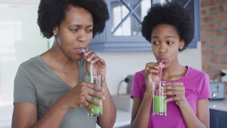 Happy-african-american-mother-and-daughter-drinking-healthy-drink-in-kitchen