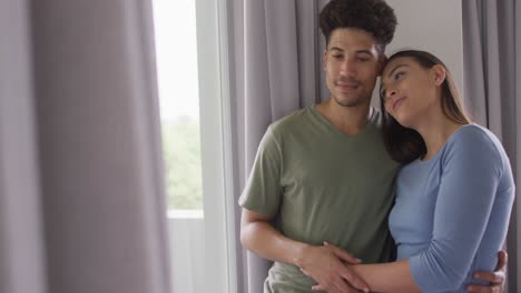 Happy-biracial-couple-embracing-and-looking-throught-window-together