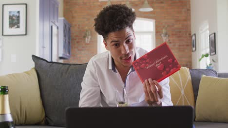 Happy-biracial-man-with-valentine-card-making-valentine's-day-video-call-on-laptop