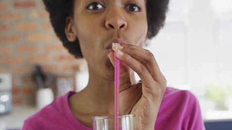 Portrait-of-happy-african-american-teenage-girl-drinking-healthy-drink-in-kitchen