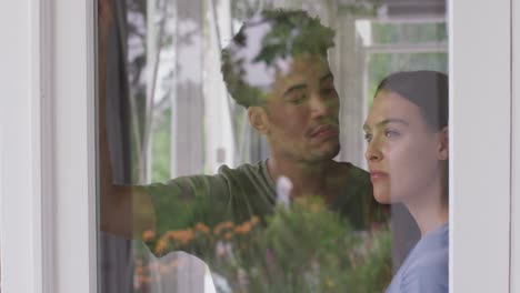 Thoughtful-biracial-couple-embracing-and-looking-throught-window-together